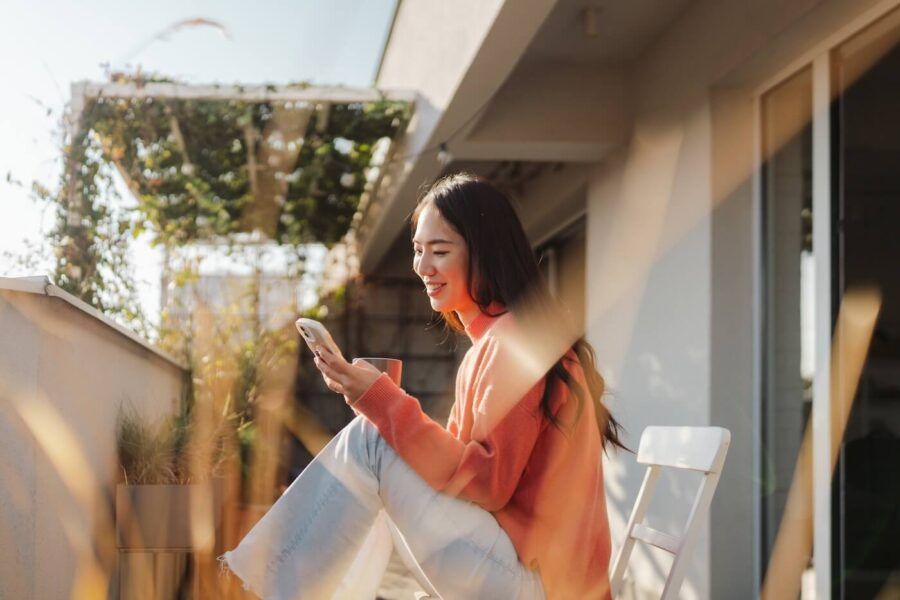 Smiling woman using her smartphone while sitting on the balcony