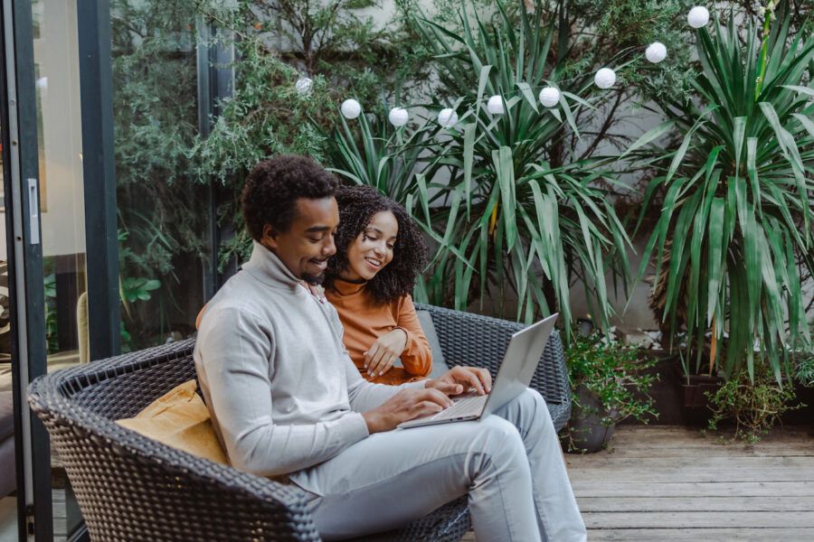 A happy young couple using a laptop in their backyard and enjoying financial freedom.