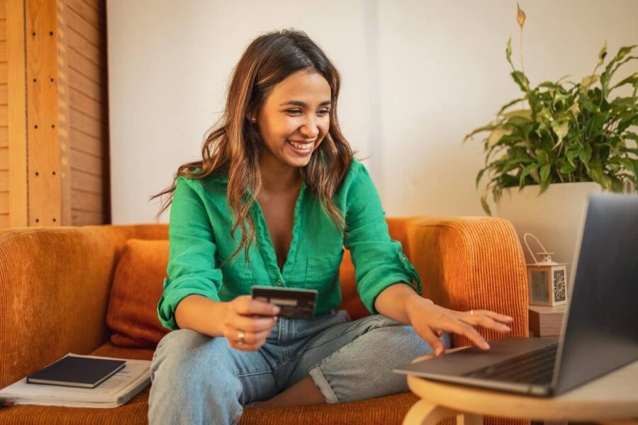 Smiling young woman using her credit card and a laptop at home