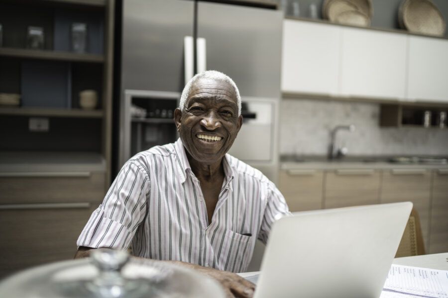 Portrait of a smiling senior man using laptop in the kitchen table