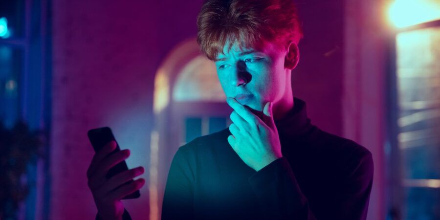 Cinematic portrait of a man holding a smartphone in neon lighted interior.