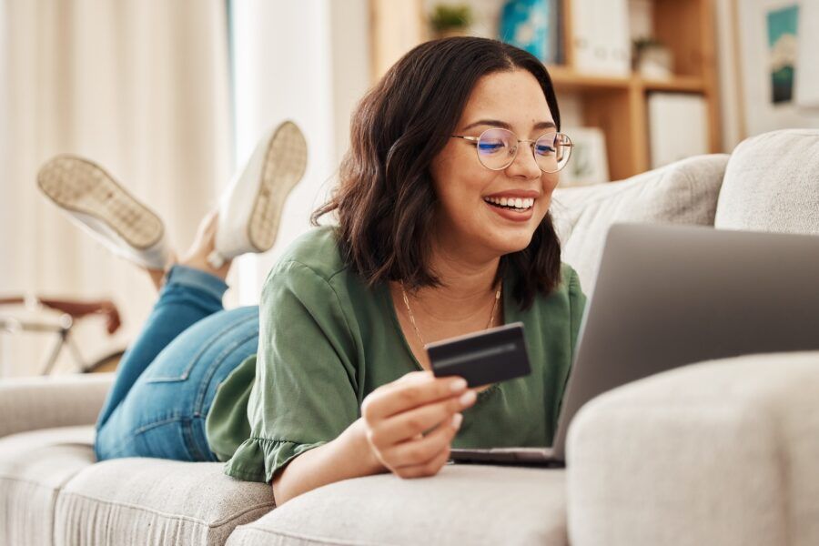 Happy woman on couch in living room with credit card and laptop.