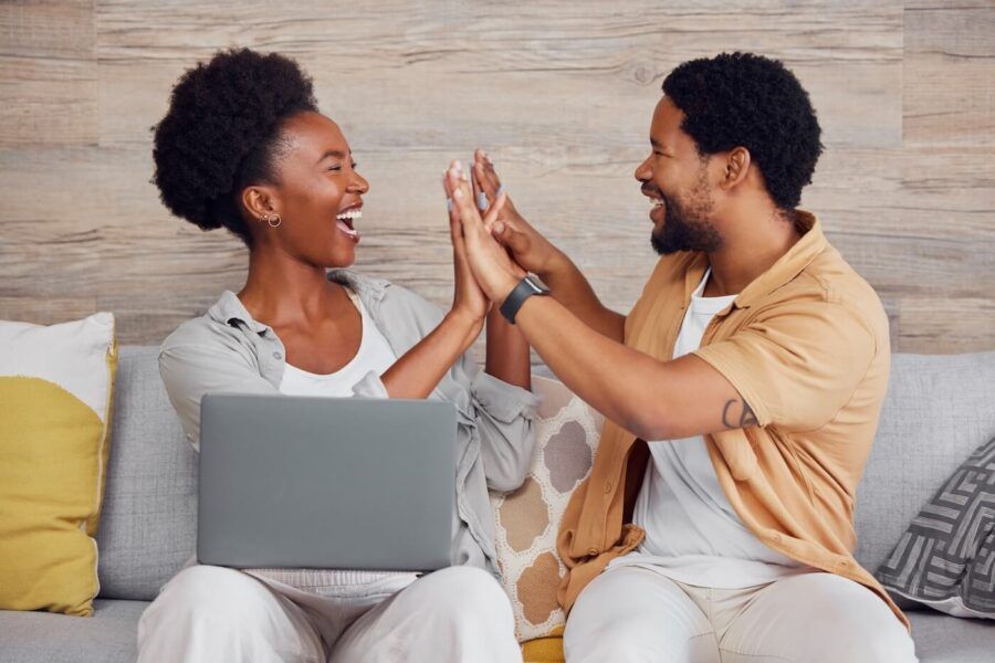 Excited couple giving high five while sitting on a sofa with a laptop