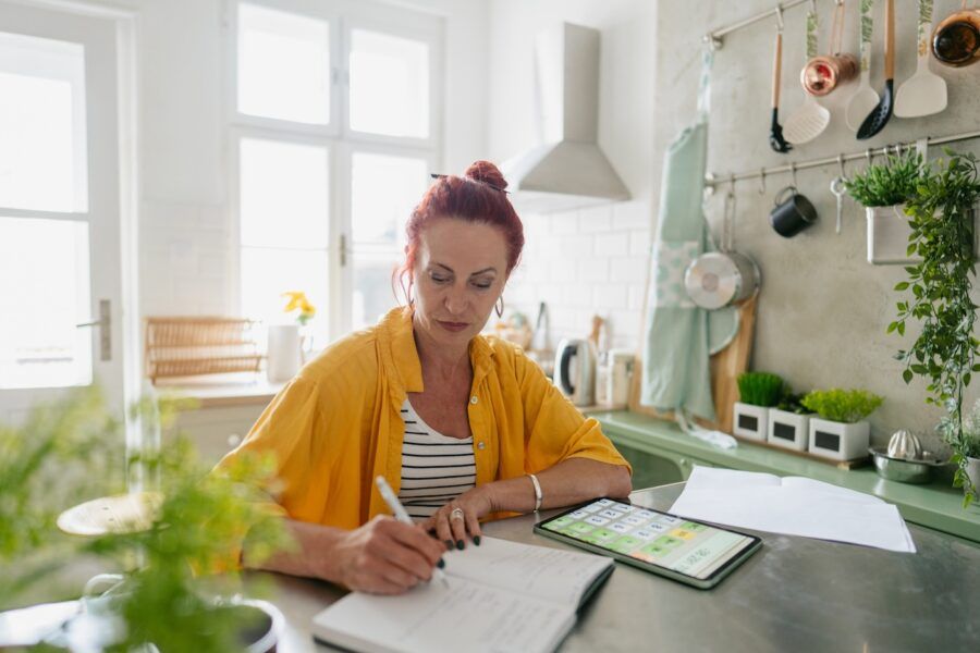 Photo of a mature woman sitting in the kitchen of her apartment, calculating her Parent PLUS loan payments.