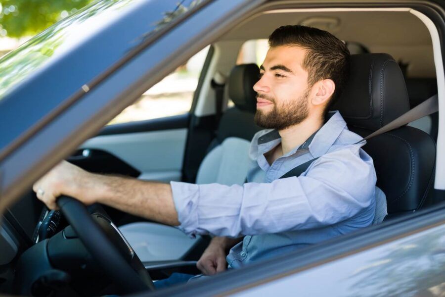 Man sitting in the driver’s seat of a car with one hand on the steering wheel, looking ahead through the windshield