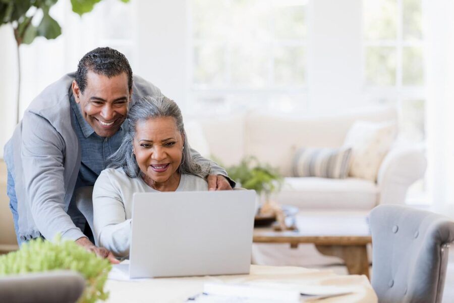A happy senior couple reviewing their finances together on a laptop in a bright, sunlit room