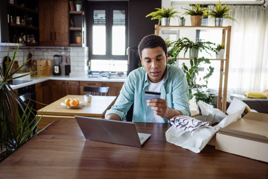 A young man at home, holding a credit card and making a savings plan on his laptop.