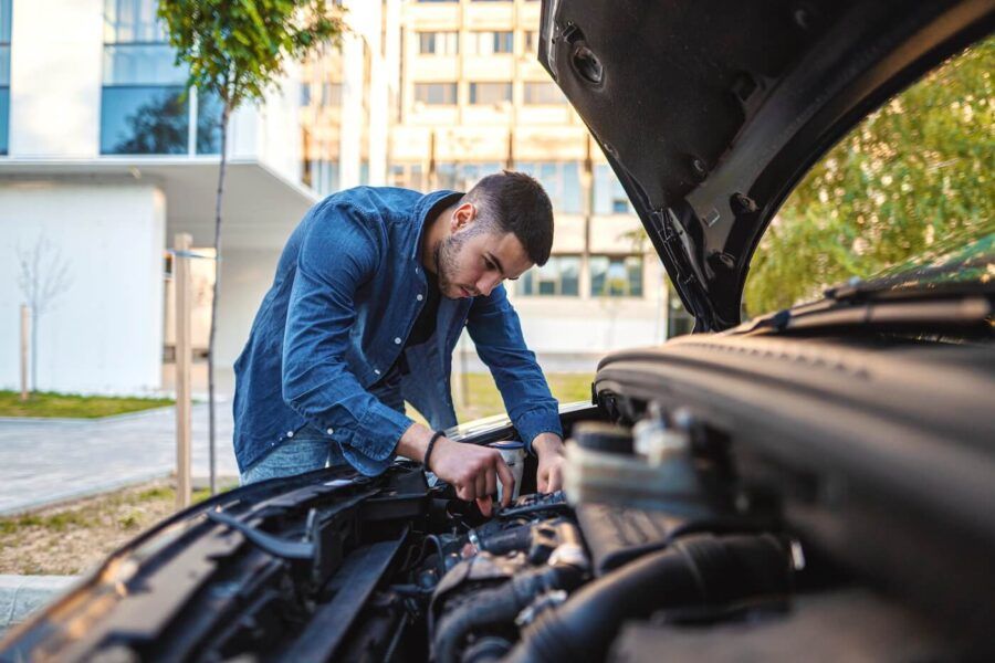 A young man working under the open hood of his car, concentrating as he attempts to repair the engine