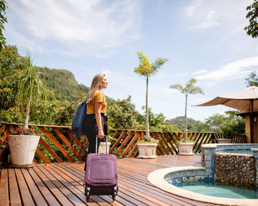 Smiling young woman with a wheeled suitcase arriving at a tourist resort in the tropics