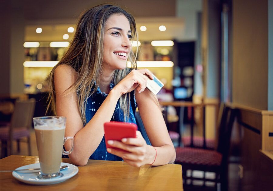 Young woman is sitting in a cafe, and shopping online using her credit card