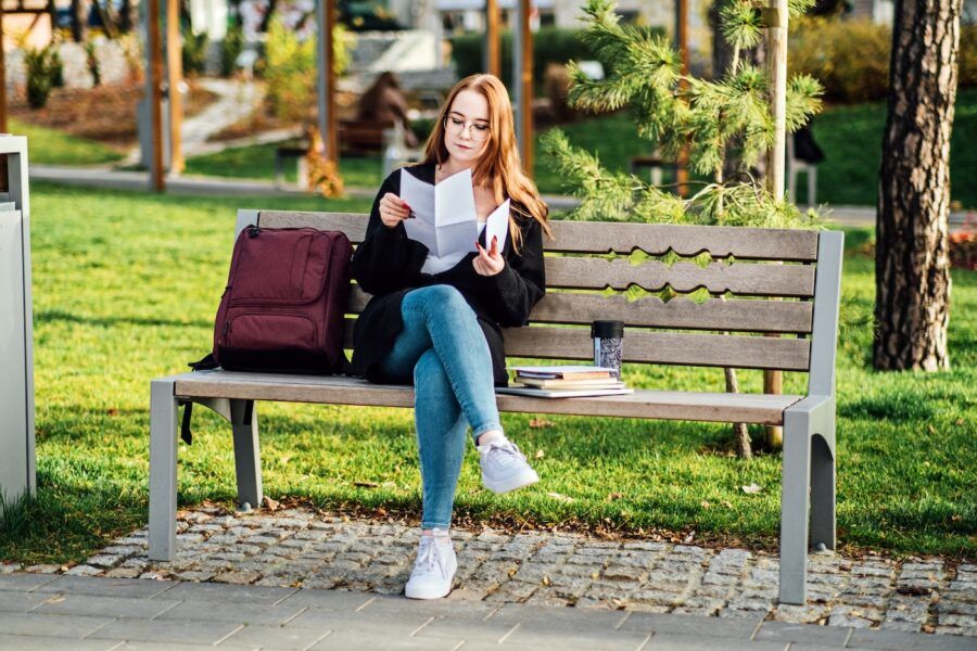 A new graduate sitting on a bench in the park with her backpack, holding a letter. She is understanding Student Loan Repayment Options.
