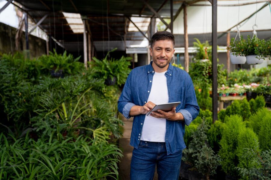 Happy business owner working at a garden center using a digital tablet and looking at the camera smiling