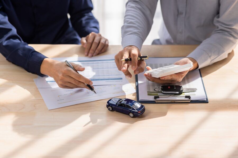 Two men looking at car documents with car keys and a small toy car on the table.