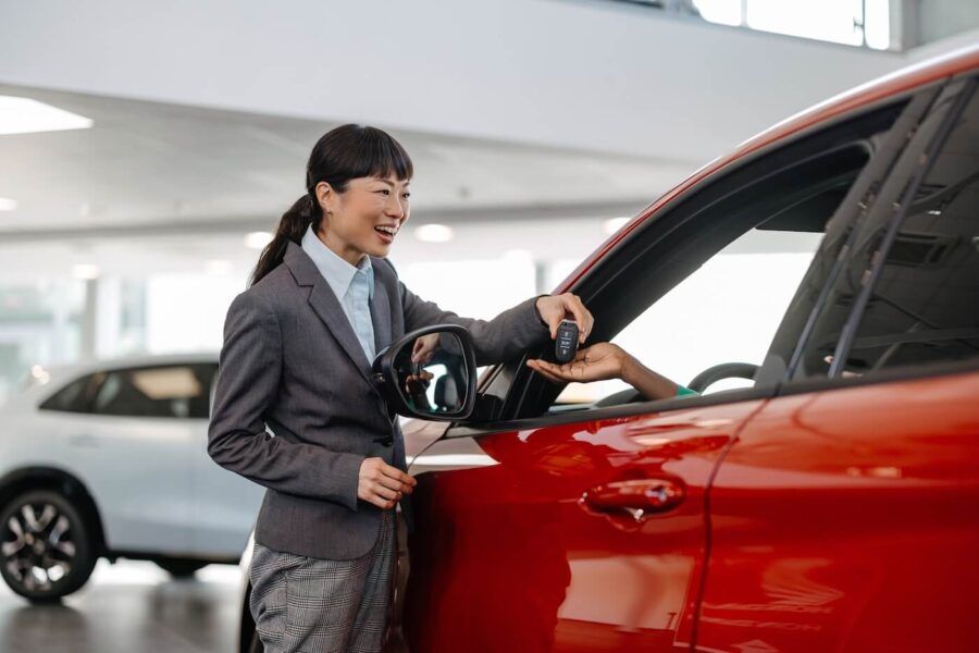 Smiling female agent giving the keys to a buyer of a red car