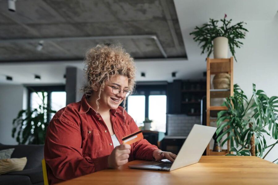 Young woman holding a debit card while checking her account balance on a laptop
