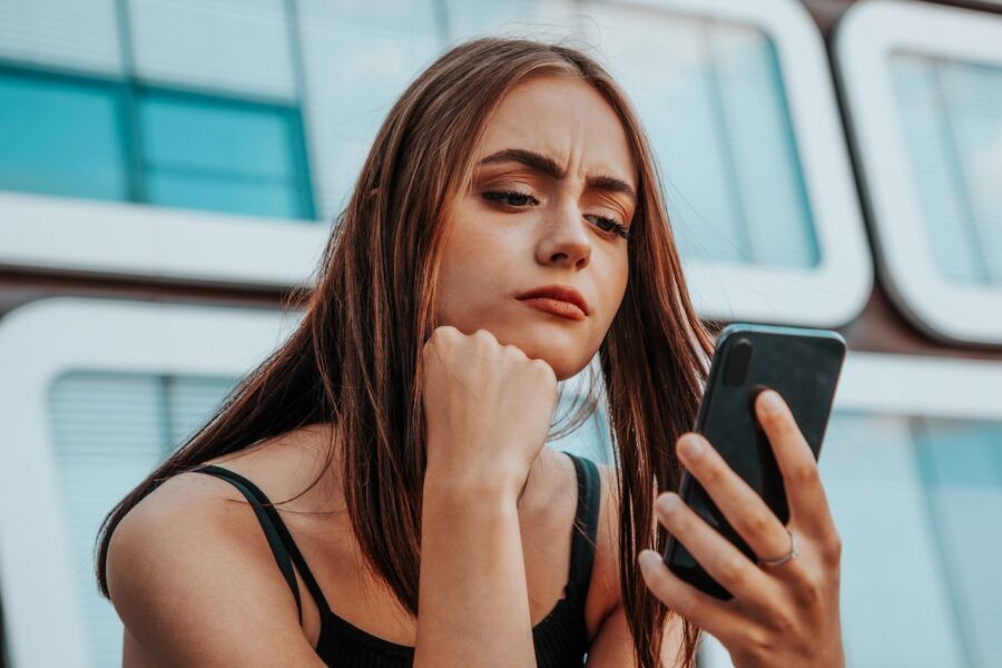 Young woman checking her mobile phone, looking skeptical and questioning the legitimacy of debt relief organizations.
