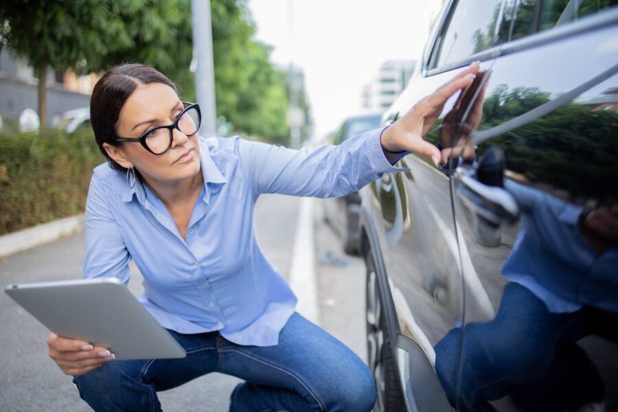 A woman holding a tablet and checking a scratch on her vehicle's door