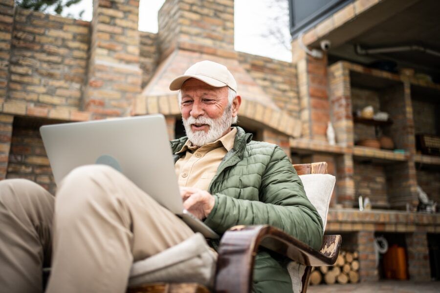 A man sits on the terrace of a cottage and works on a laptop.