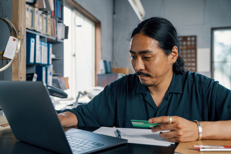 Man checking credit score with a credit card in his hand. He is sitting in front of a computer.