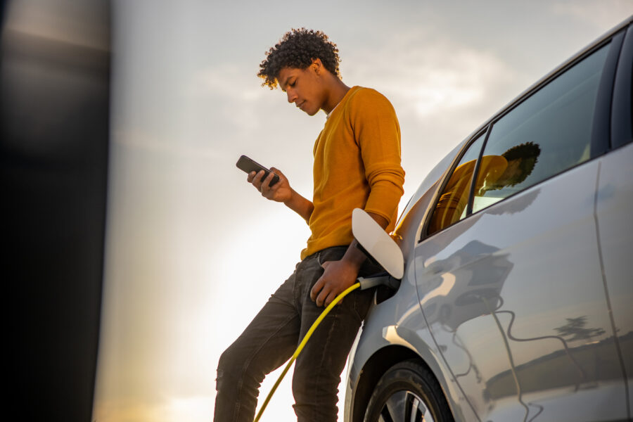 Man charging his EV car considers a car title loan while looking at his phone.