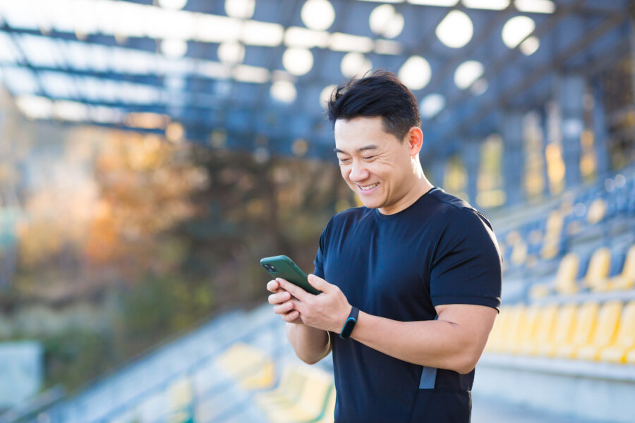 A healthy man checks his finances on a mobile phone after a workout while sitting outdoors.