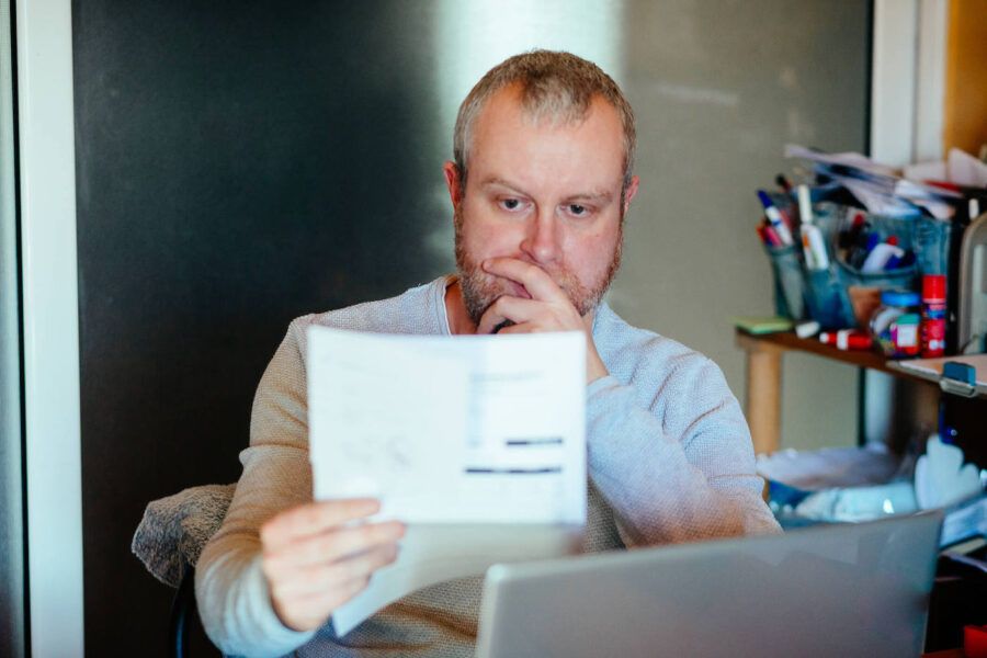 Man looking seriously at piece of paper with hand over mouth.