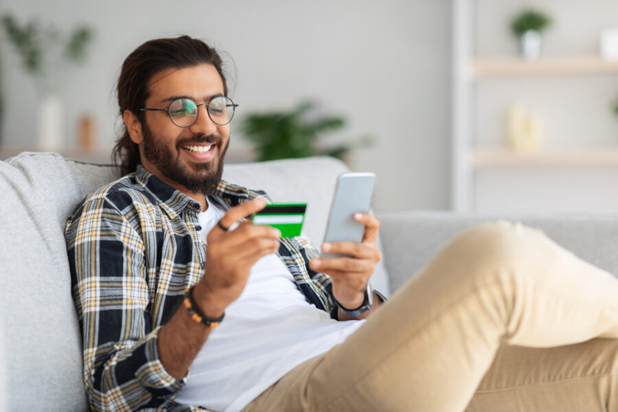Man sitting on couch using his phone to budget with his credit card