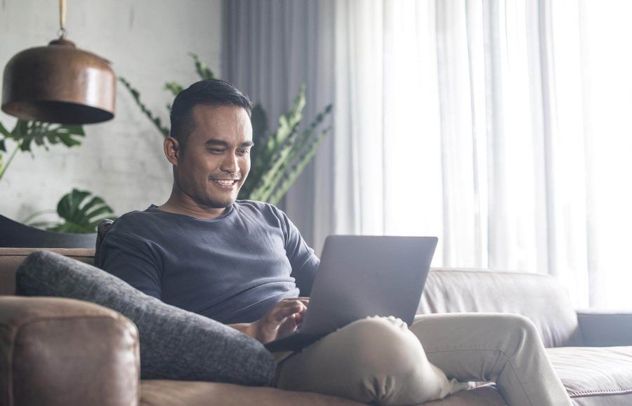 A man sitting on a couch with his laptop smiling.