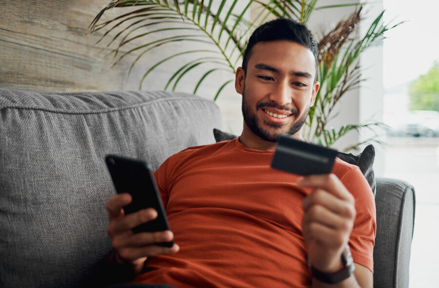 Happy man laying on the couch using credit card for buy now pay later