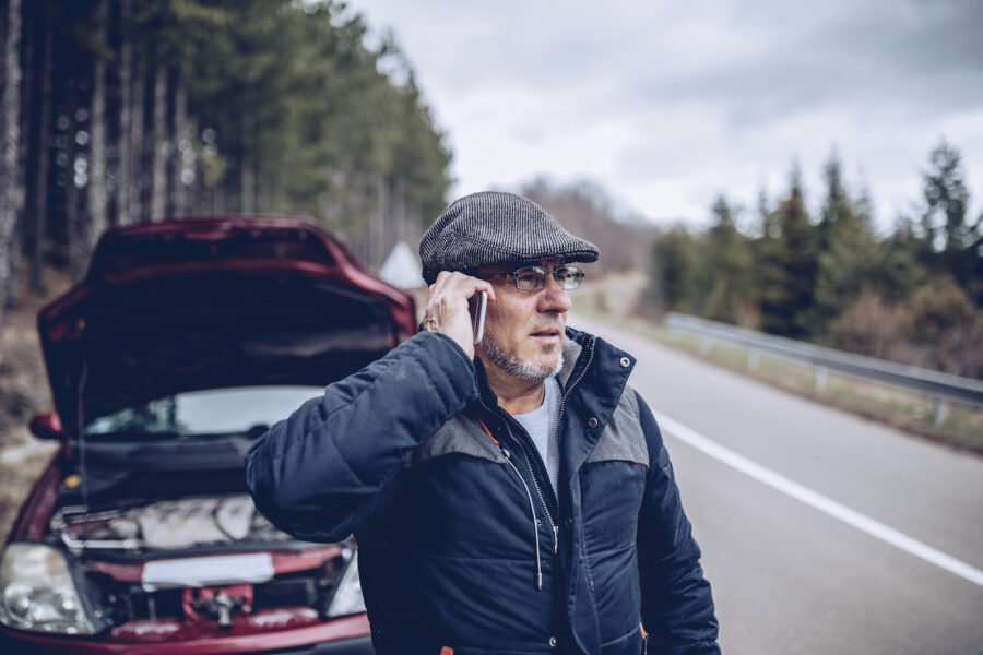 A man having car problems on the road in the mountains, talking on mobile phone.