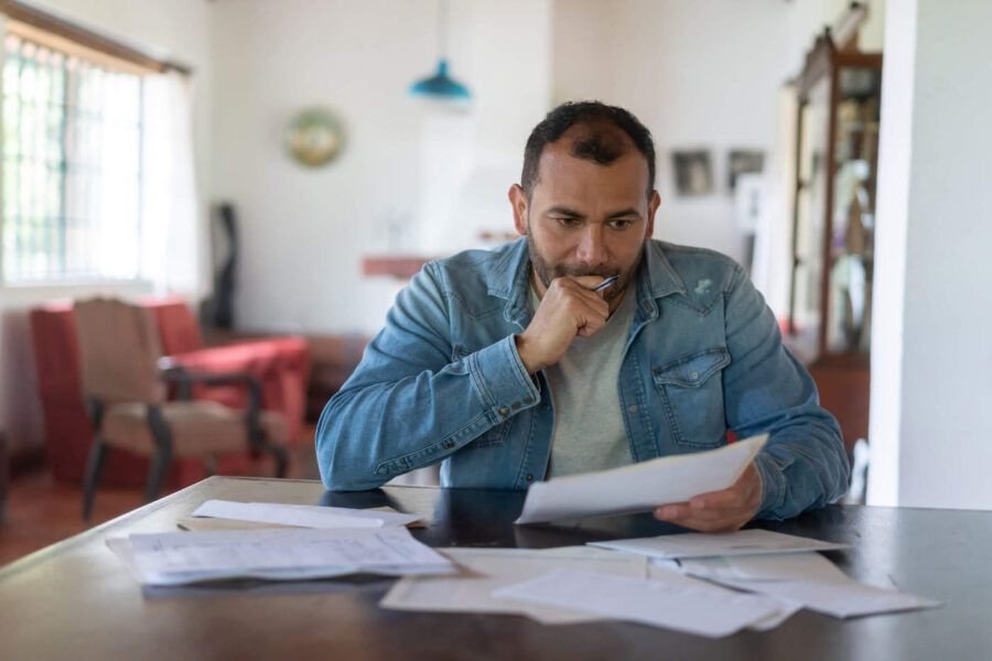 pensive man looking mildly concerned while reviewing papers seated at a desk in living room