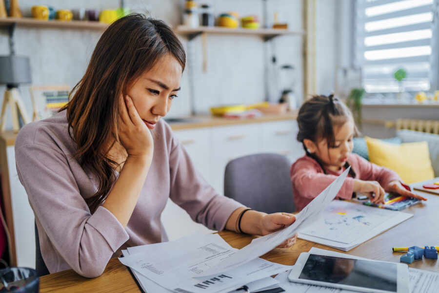 Stressed mother going through her finances next to her child, who is playing with crayons.