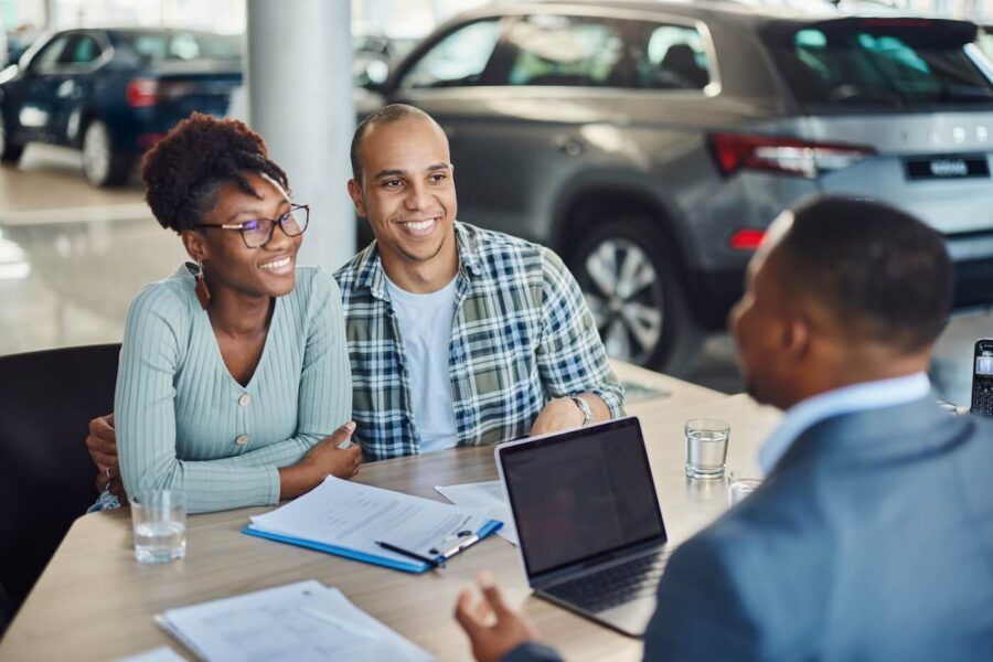 Happy couple discussing auto loan terms with a male sales agent in a dealership