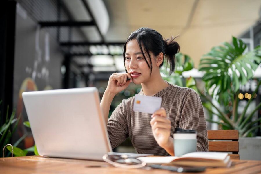 Focused young woman using her laptop in the cafe while holding a credit card