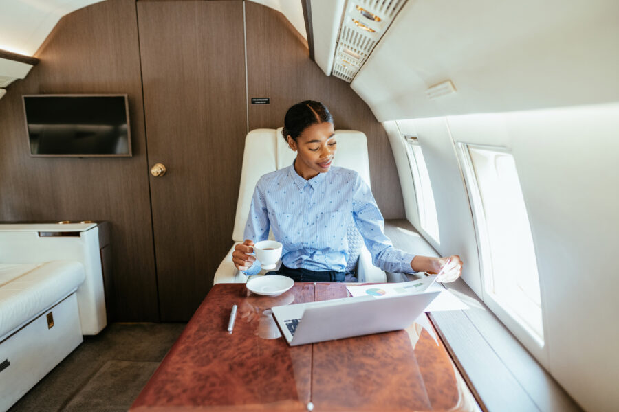 Wealthy womanusing private luxury jet to travel to destination, looking over private banking paperwork on laptop