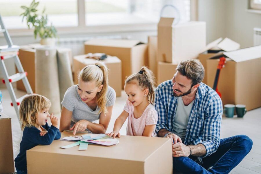 Family of four sitting on the floor of the new living room surrounded by moving boxes and choosing the wall paint color
