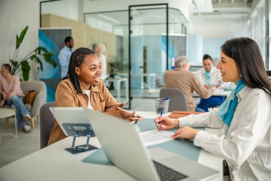 Smiling female customer reviewing certificate of deposit (CD) options with a female bank representative in a modern bank office