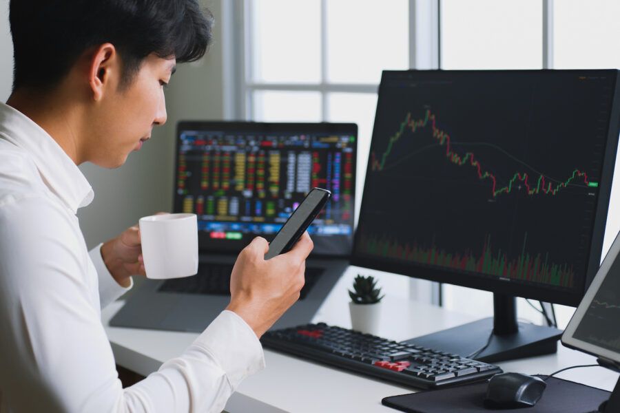 Young investor buying stocks, holding phone and coffee