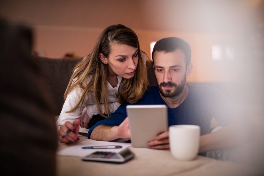 Couple sitting in their living room and checking their finances on digital tablet.