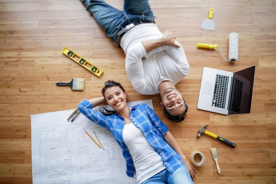Portrait of a happy couple deciding whether to remodel or move, laying on the floor surrounded by tools and smiling at the camera.