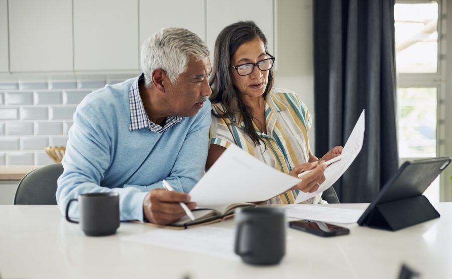 An older couple is sitting at their kitchen table reviewing financial documents.