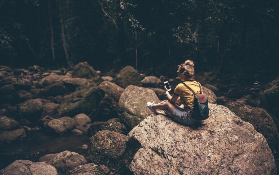 A woman sitting on rocks in the woods, using her phone.