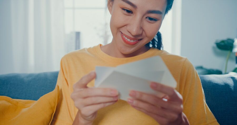 Young woman excited opening envelope on couch in living room at home.