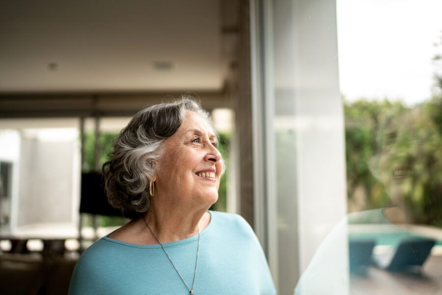 Senior woman looking through window, enjoying her home