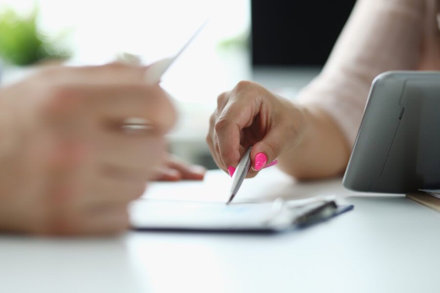 A hand with a bright pink manicure pointing at documents with a pen.