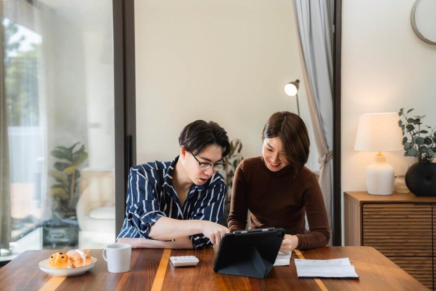 Young couple sitting at home, planning their finances and discussing something on a tablet