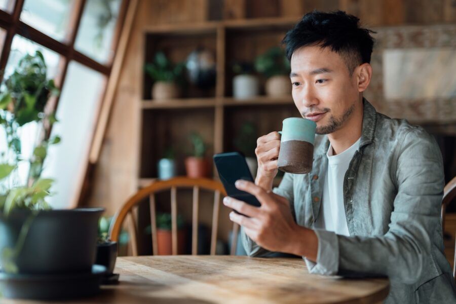 A man managing online banking with mobile app on smartphone, taking care of his money and finances while relaxing at home with a cup of coffee.