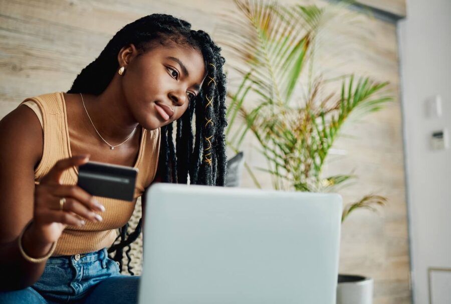 Pensive young woman sitting on a couch with an open laptop and holding a credit card