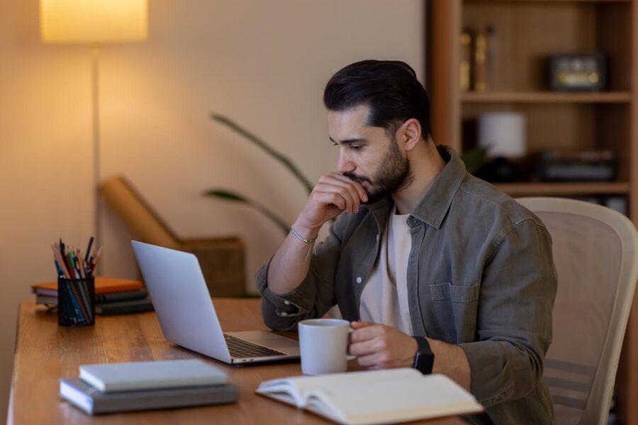 Focused young man using a laptop and holding a mug in a home office