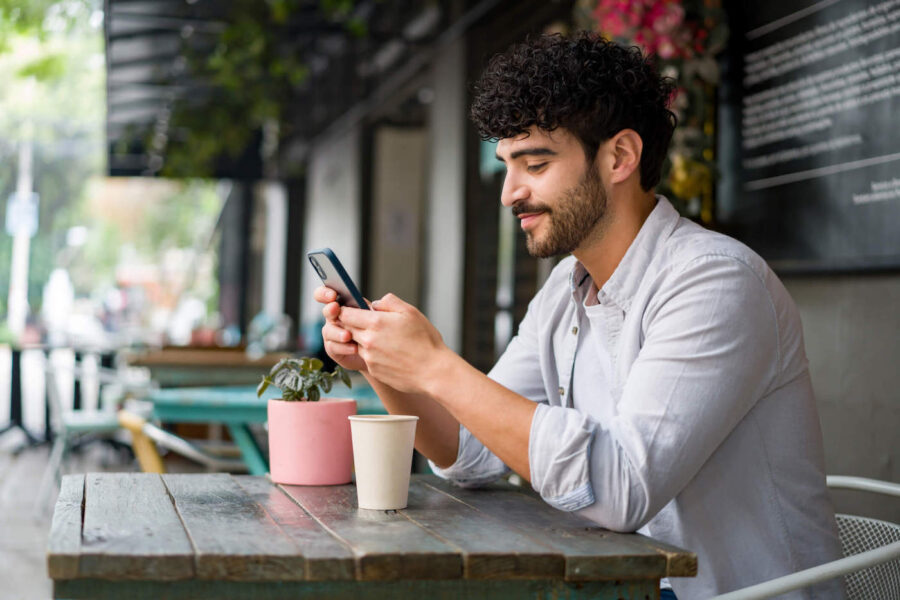 Smiling man seated outside looking at phone.